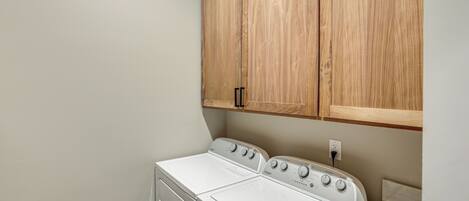 A laundry room with a front-loading washer and dryer, wooden cabinets above, and a white countertop.
