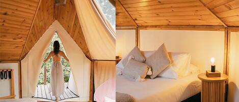 Una carpa con interior de madera, una cama con almohadas y una mesita de noche con una lámpara.
