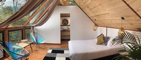 Een gezellige slaapkamer met een puntig dak, een bed, een schommelstoel en uitzicht op de omgeving.