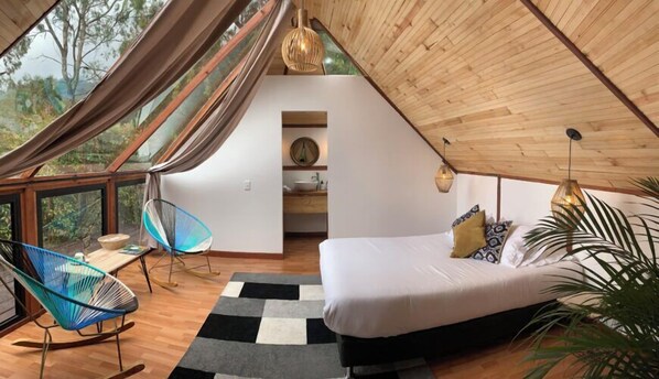 Une chambre à coucher accueillante, avec un toit en forme de triangle, comprenant un lit, un fauteuil à bascule et une vue sur l’extérieur.