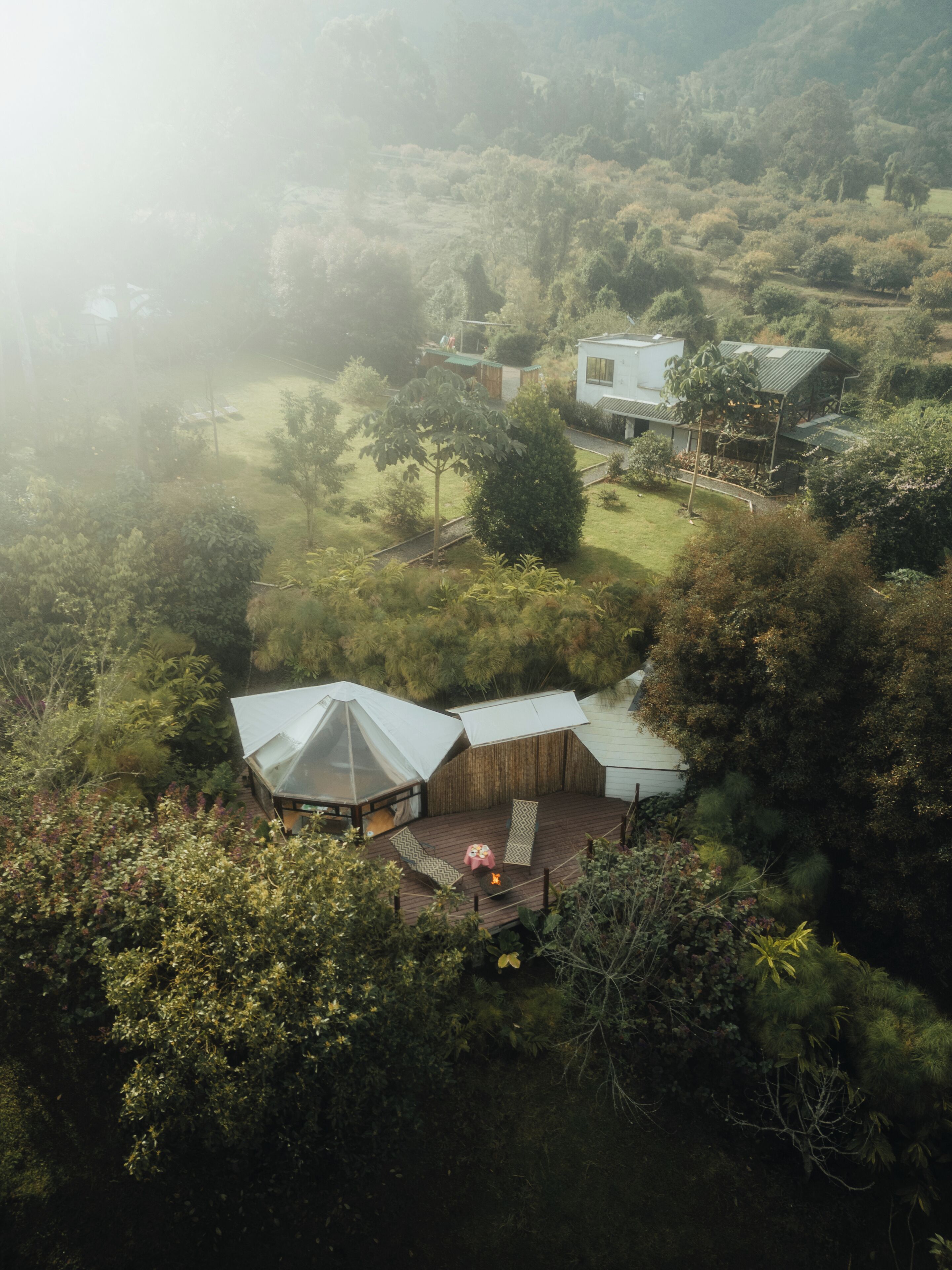 A secluded, rustic cabin surrounded by dense forest, featuring a wooden deck and a large, white tent-like structure.