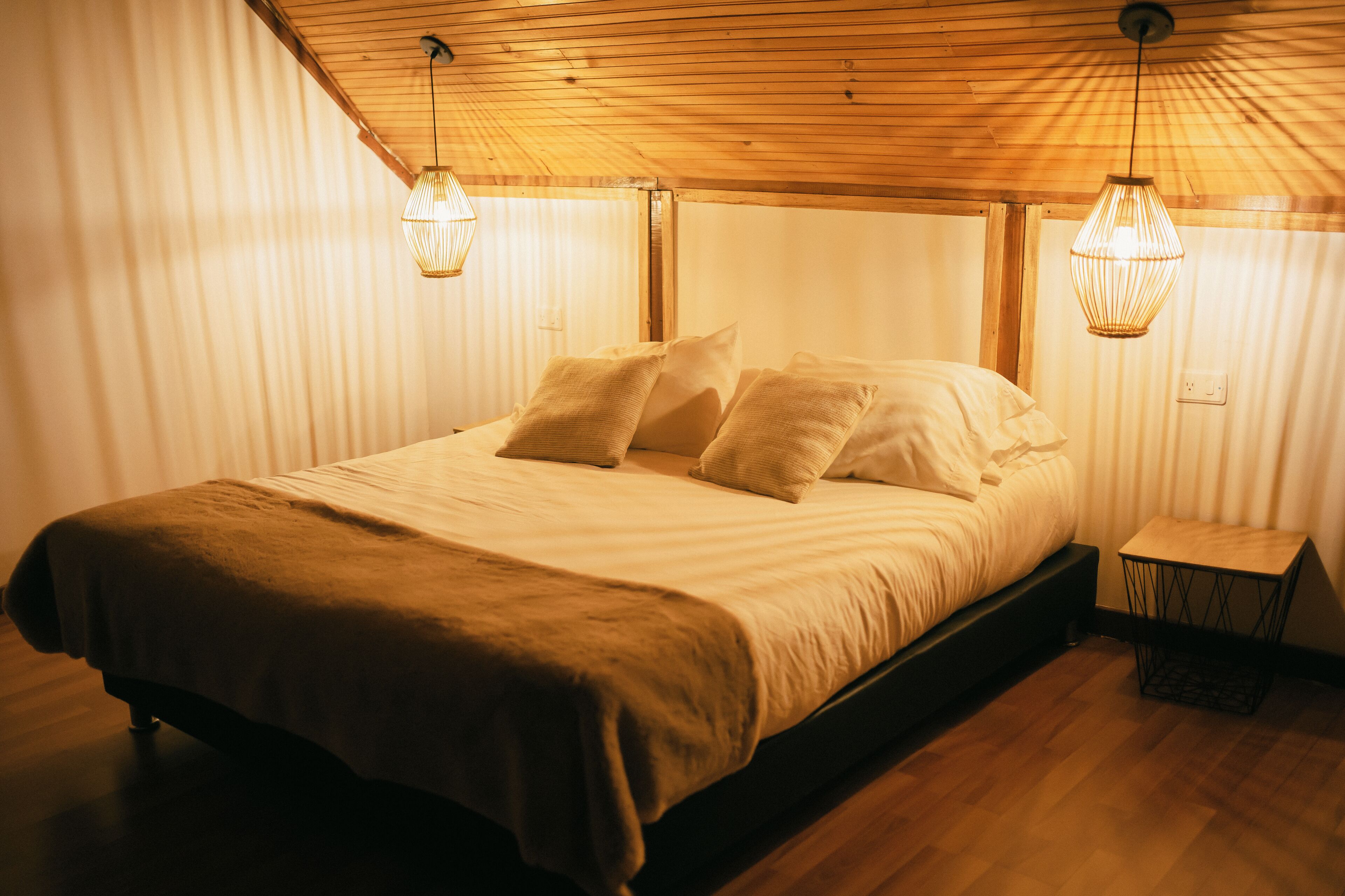 A neatly made bed with a wooden headboard, two bedside lamps, and a small wooden nightstand.