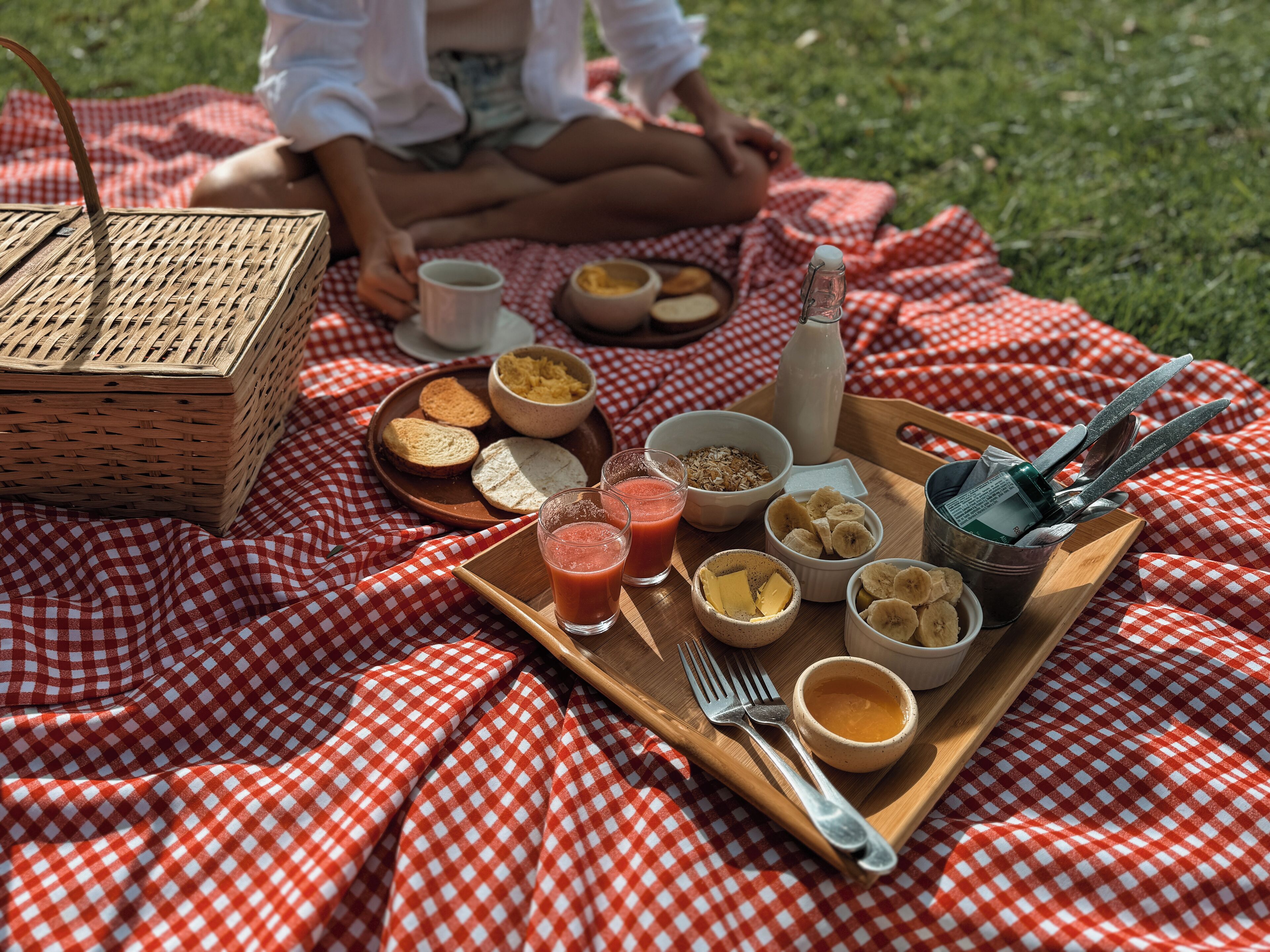 Una preparación para picnic con una manta a cuadros, una cesta y una bandeja con comida y bebidas.