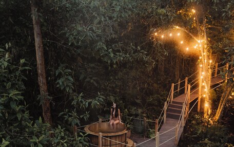 A wooden deck with a hot tub and a small table, surrounded by dense foliage.