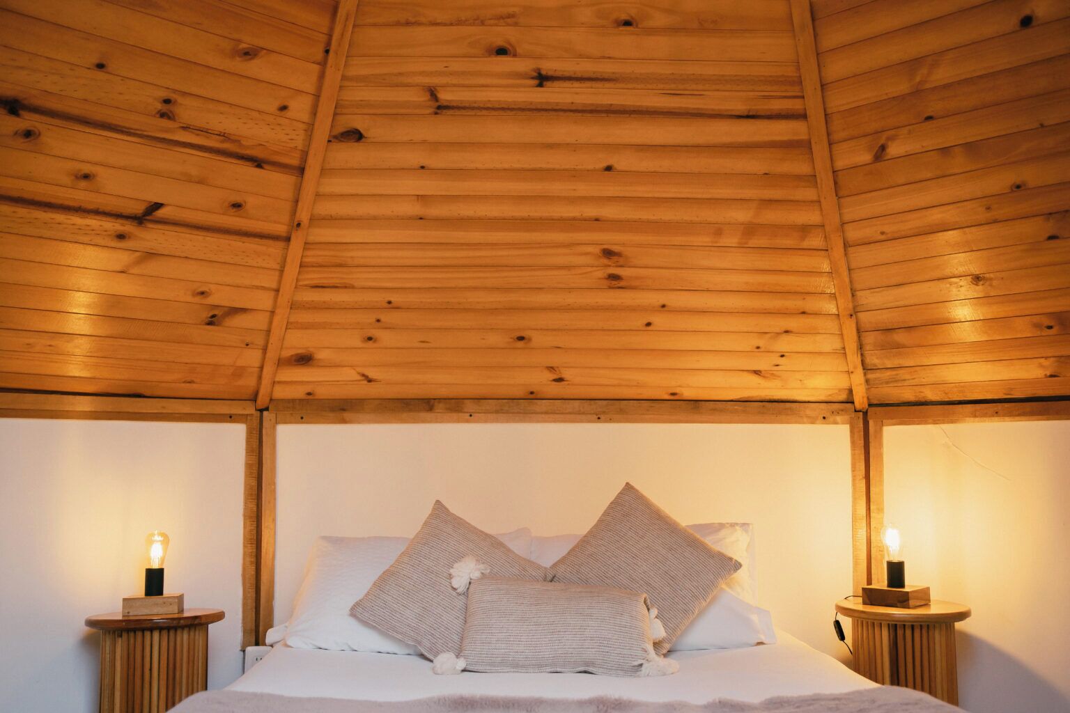 Techo de madera en una habitación con una cama, dos mesitas de noche y dos lámparas de pared.