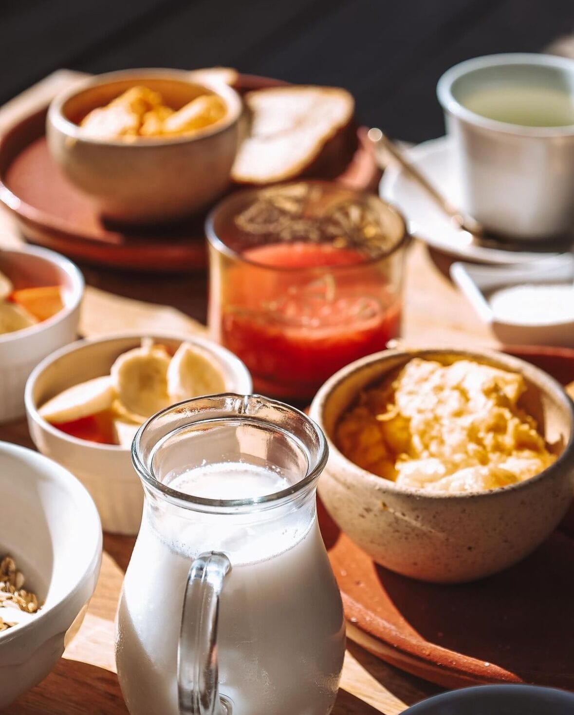 A breakfast setting with various dishes including a pitcher of milk, bowls of food, and a glass of red beverage.