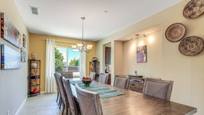 A dining area with a wooden table, chairs, and a chandelier. There are decorative plates on the wall and a shelf with items. - Family Home w/ Patio & Fenced Yard in Brentwood (Brentwood)