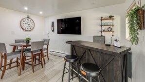 A modern kitchen with a wooden bar, a round dining table with chairs, a wall-mounted clock, and a TV. - Walk to Dtwn Flagstaff: Home w/ Great Outdoor Area (Flagstaff)