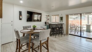 A modern kitchen with a dining area, a TV mounted on the wall, and a sliding glass door leading to an outdoor patio. - Walk to Dtwn Flagstaff: Home w/ Great Outdoor Area (Flagstaff)
