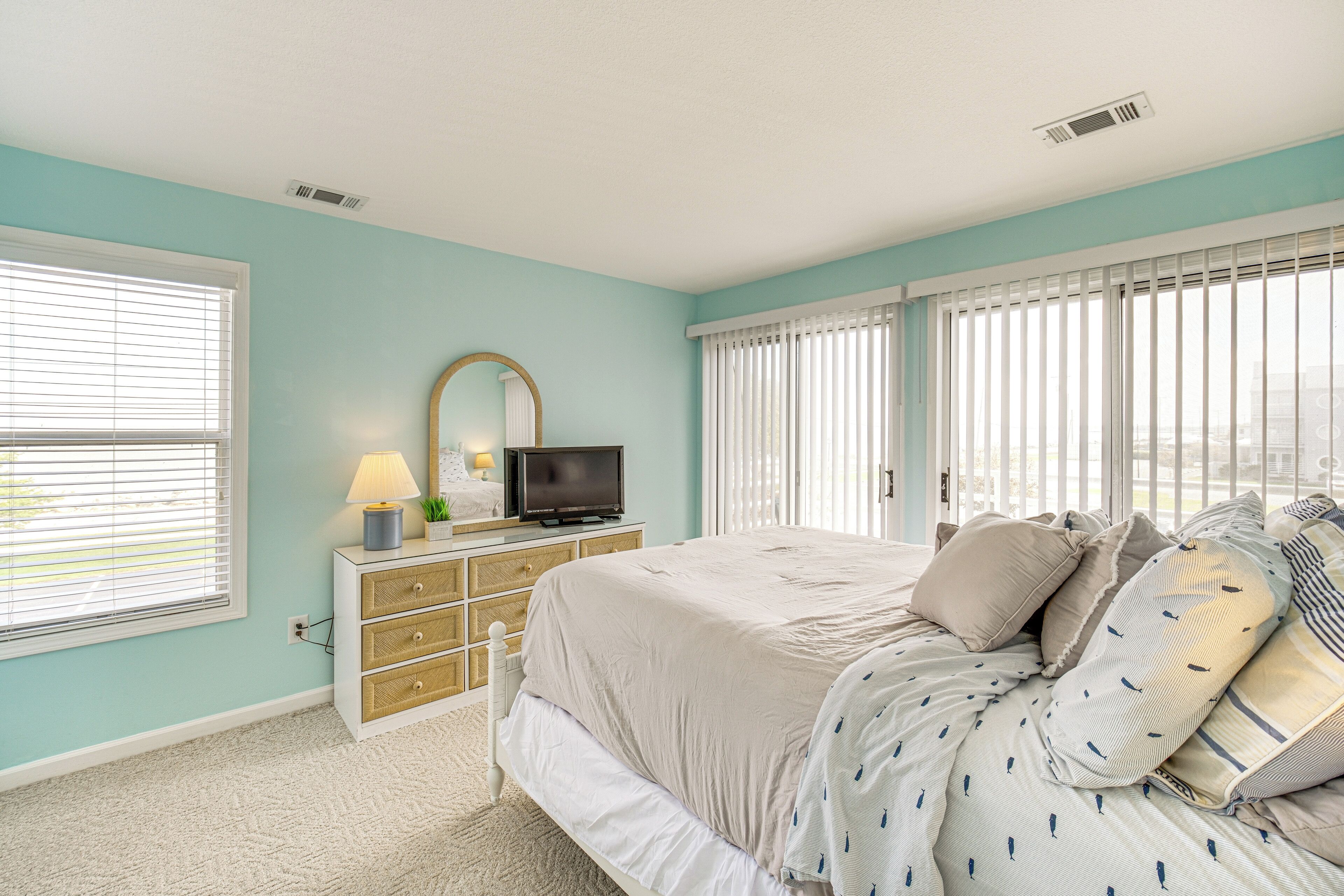 A bedroom with a bed, dresser, TV, and windows.