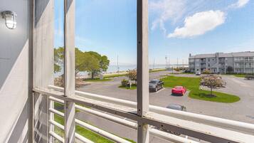 Blick durch ein Fenster mit Metallgitter auf einen Parkplatz mit einem roten Auto, ein mehrstöckiges Gebäude und einen klaren Himmel.