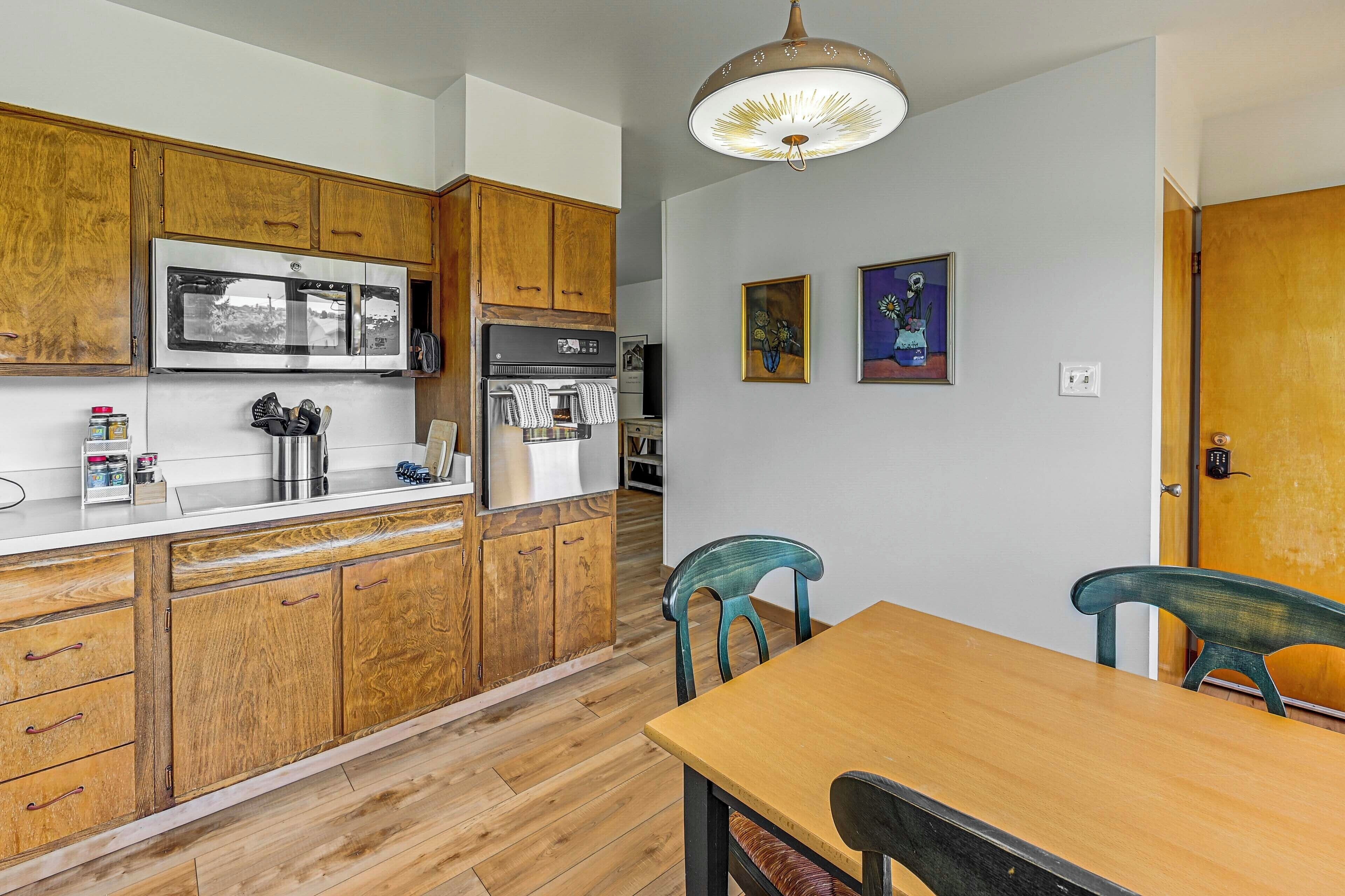 A kitchen with wooden cabinets, a stainless steel refrigerator, a wooden dining table with chairs, and a pendant light.
