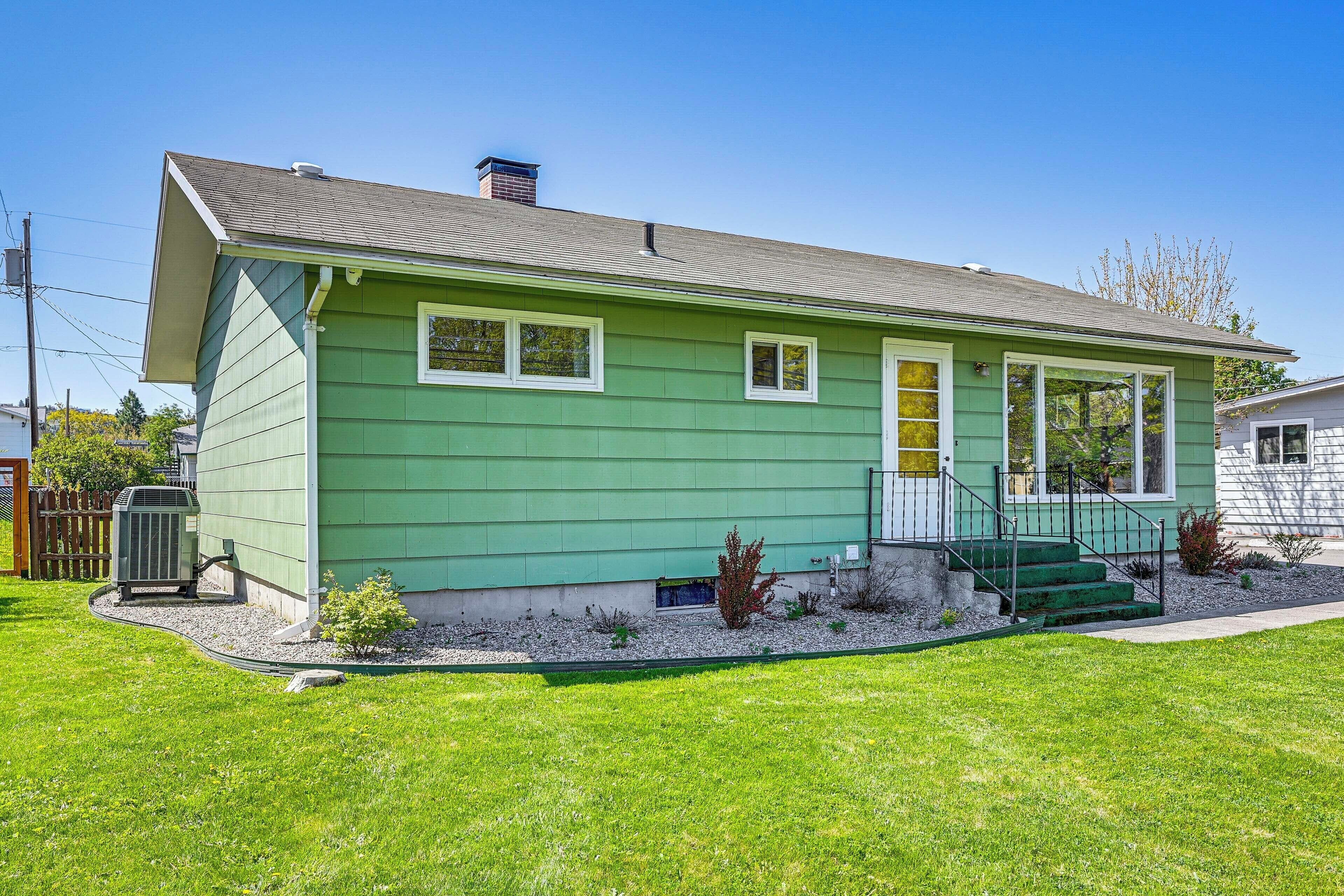 A green single-story house with a front porch, a small garden, and a visible air conditioning unit.