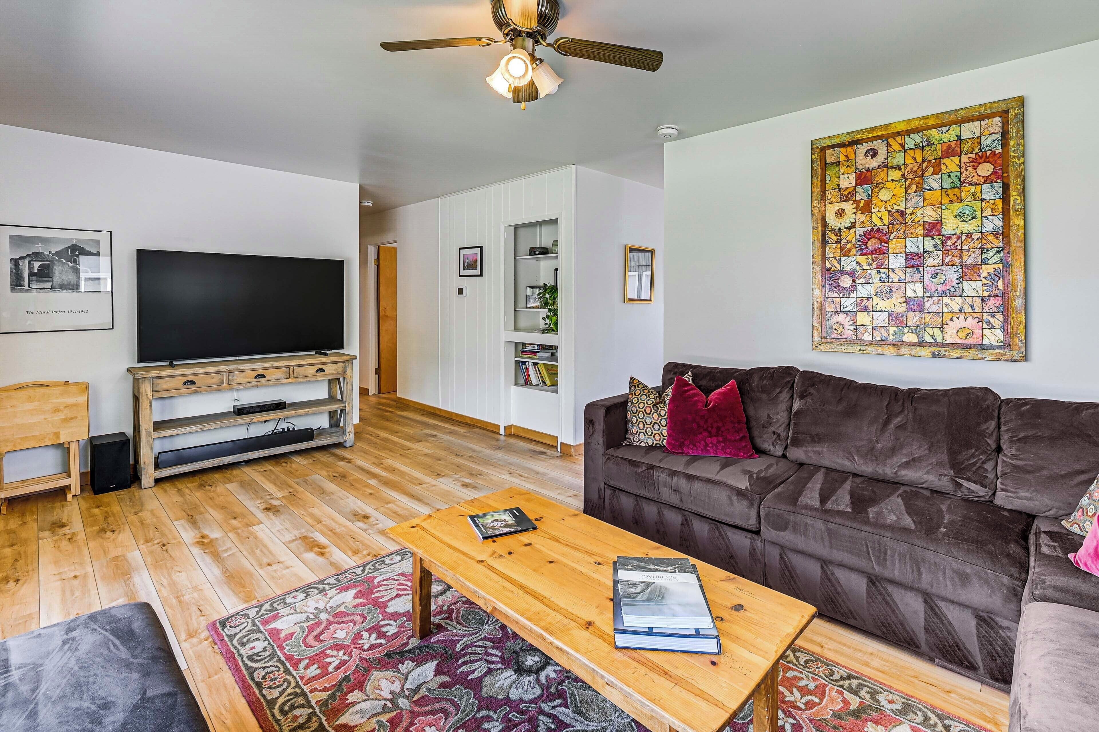 Ein Wohnzimmer mit Flachbildfernseher, Couchtisch aus Holz, braunem Sofa und Deckenventilator.