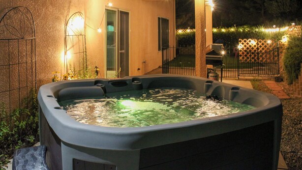 Un bain à remous installé dans un espace patio extérieur, surmonté d’une pergola et illuminé de guirlandes lumineuses.
