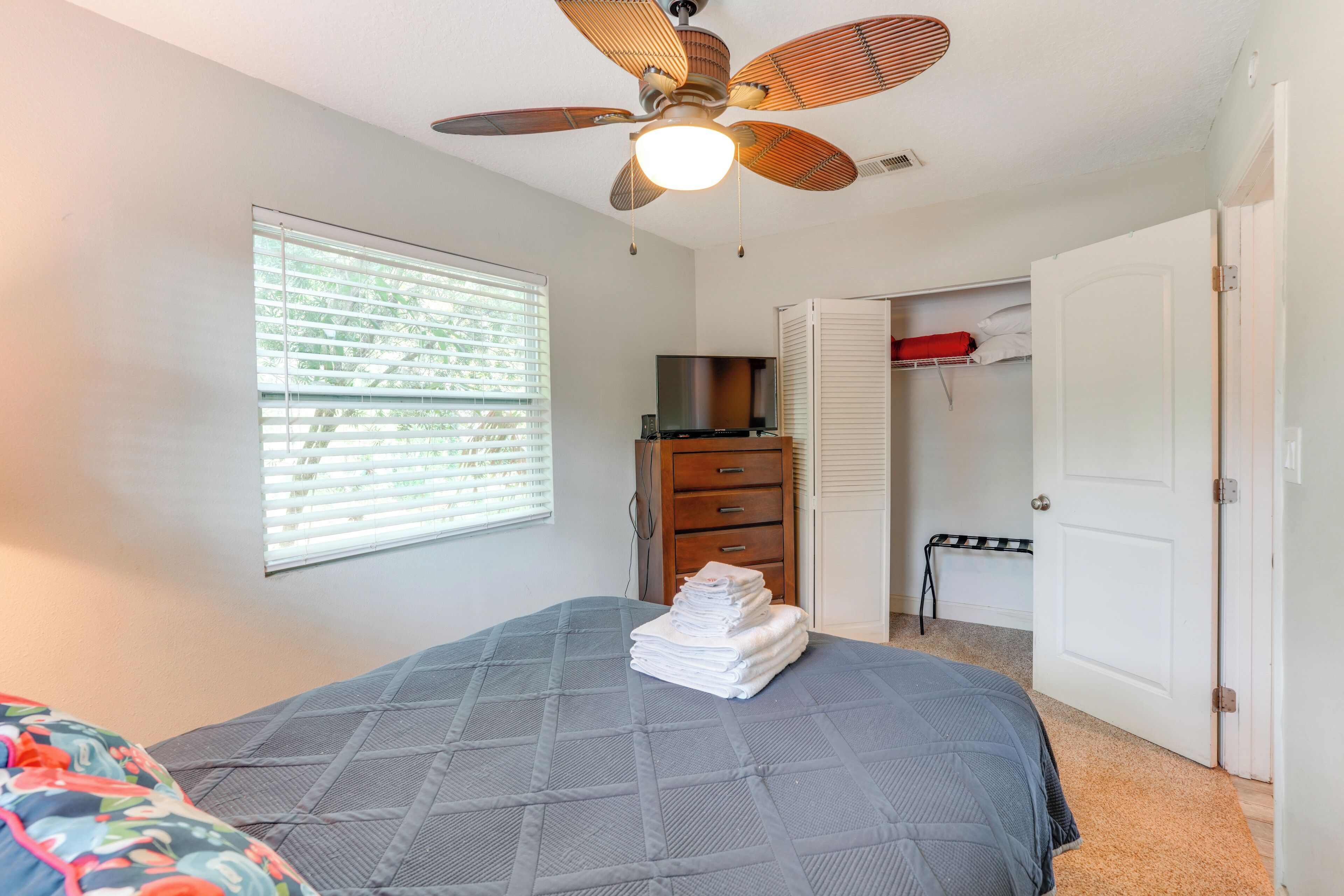Ein Schlafzimmer mit Bett, Deckenventilator, Fernseher, Kleiderschrank und einem Fenster mit Jalousien.