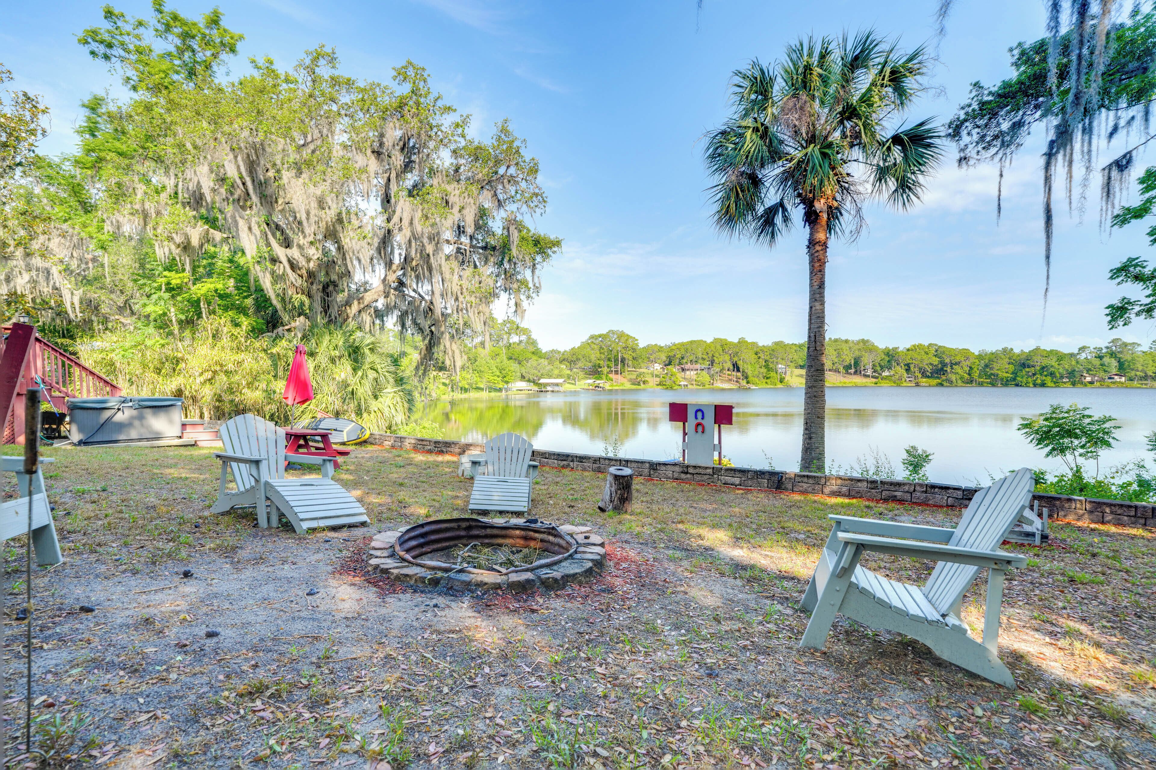 An outdoor seating area with Adirondack chairs, a fire pit, and a view of a lake surrounded by trees.