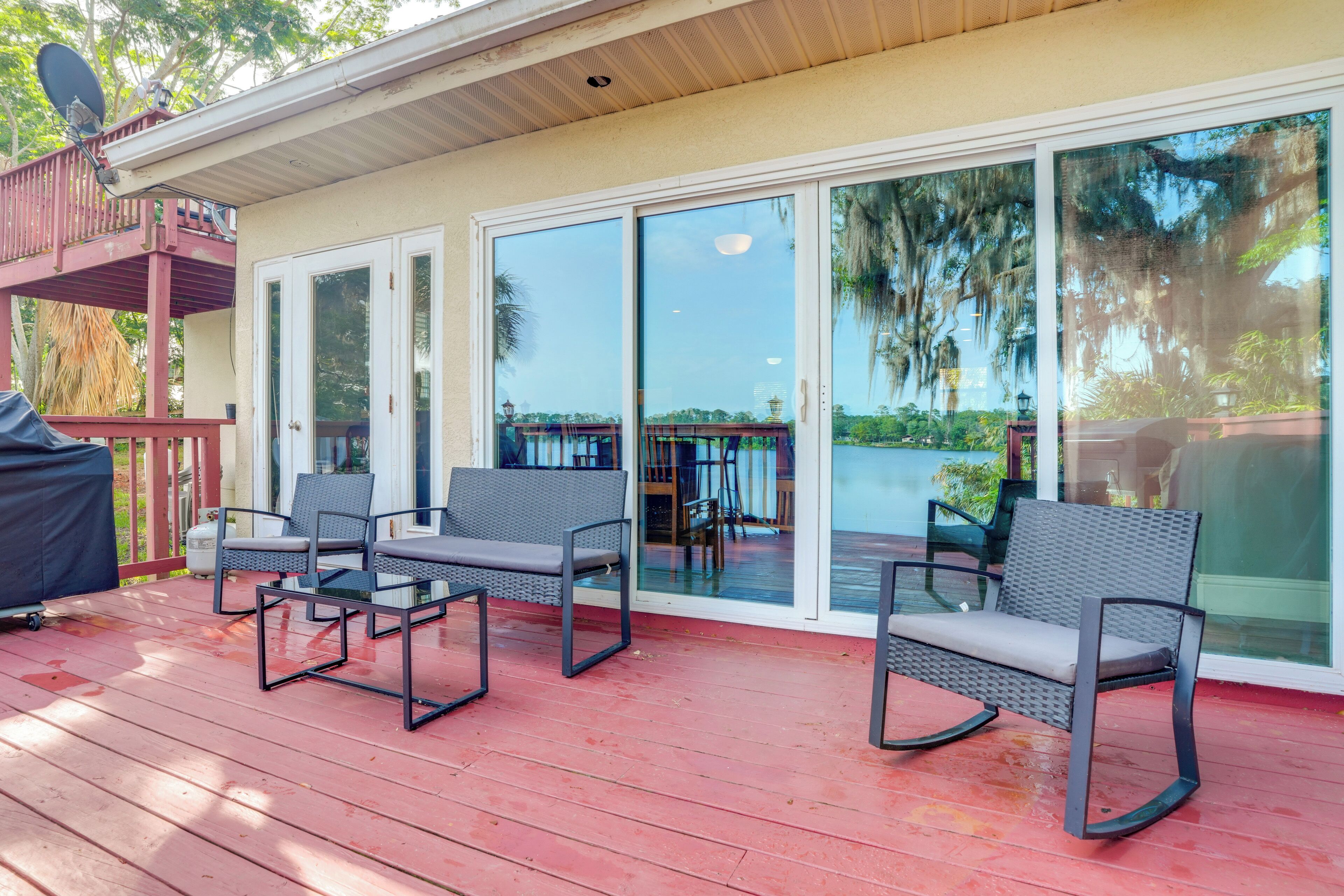 A covered outdoor deck with two chairs and a grill, a sliding glass door leading to a covered patio, and a satellite dish on the roof.