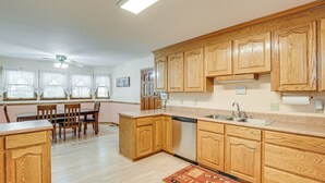 Una cocina con armarios de madera, lavavajillas, fregadero y comedor con sillas y mesa.