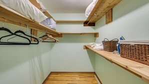 Una habitación pequeña y estrecha con literas de madera, suelo de madera y un estante con cestas y perchas.
