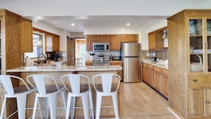 A modern kitchen with wooden cabinets, stainless steel appliances, and a central island with bar stools. - Unreal Mountain Views w/ Hot tub Near Charming Jim Thorpe & Blue Mountain Skiing (Jim Thorpe)