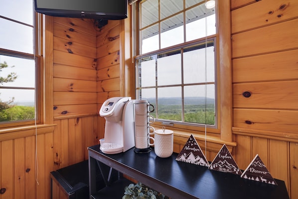 A wooden cabin interior with a coffee maker, mug, and a table with mountain-themed decorations.