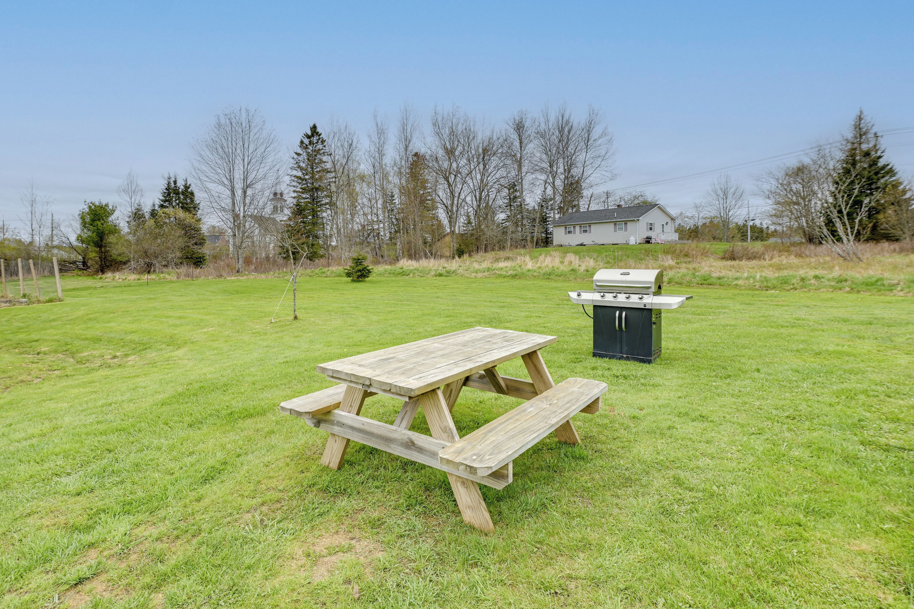 A picnic table and grill in a grassy backyard with a house in the background.