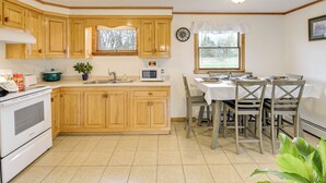 A kitchen with wooden cabinets, a microwave, a stove, and a dining area with chairs and a table. - Day Trip to Acadia: Quiet Coastal Maine Escape (Harrington)