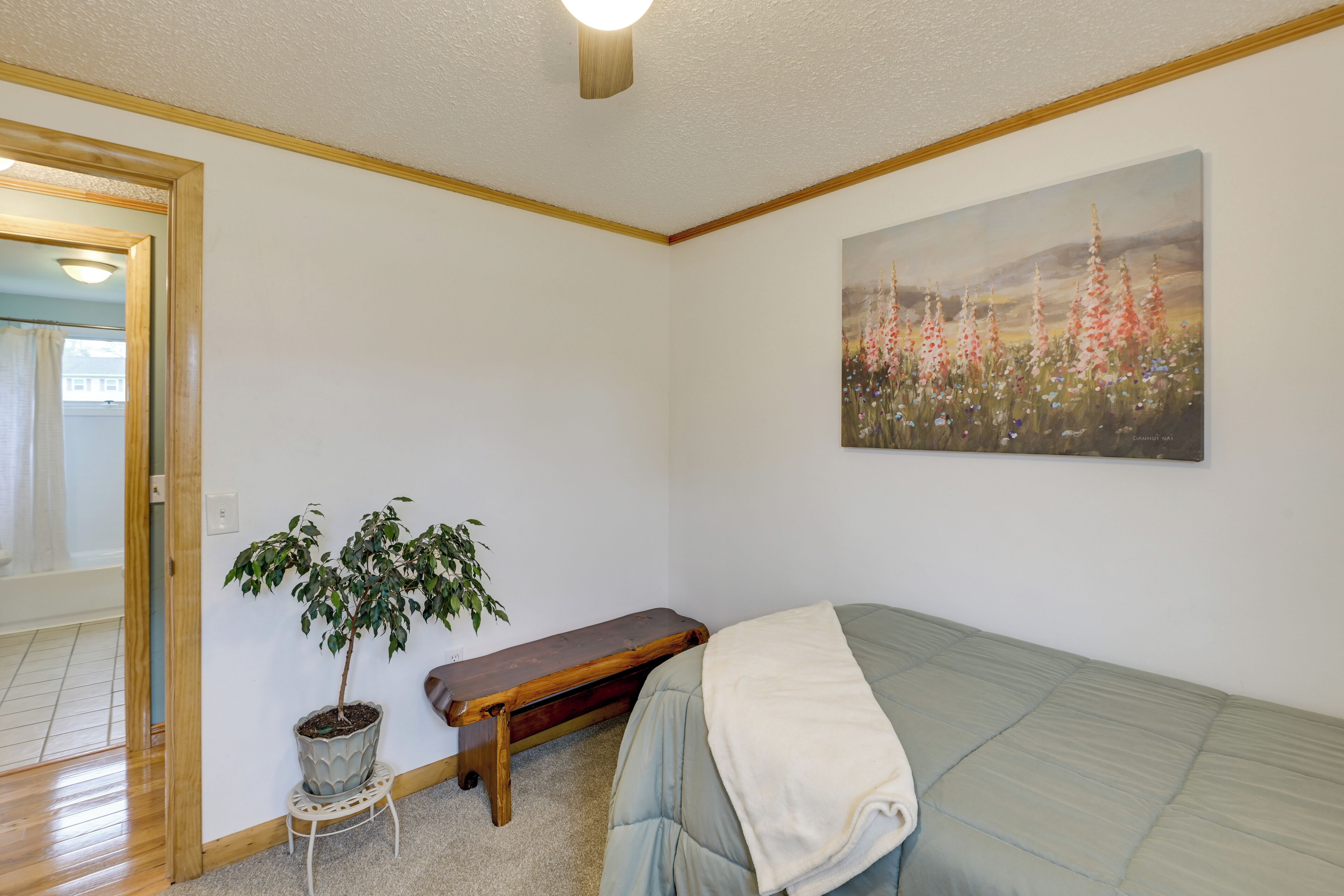 Ein Schlafzimmer mit einem Bett, einer Bank, einer Topfpflanze und einem Bild an der Wand.