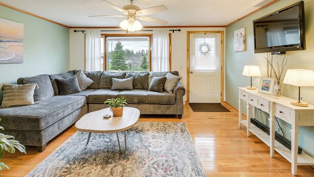 A living room with a sectional sofa, a coffee table with a plant, a television, and a console table with lamps. - Day Trip to Acadia: Quiet Coastal Maine Escape (Harrington)