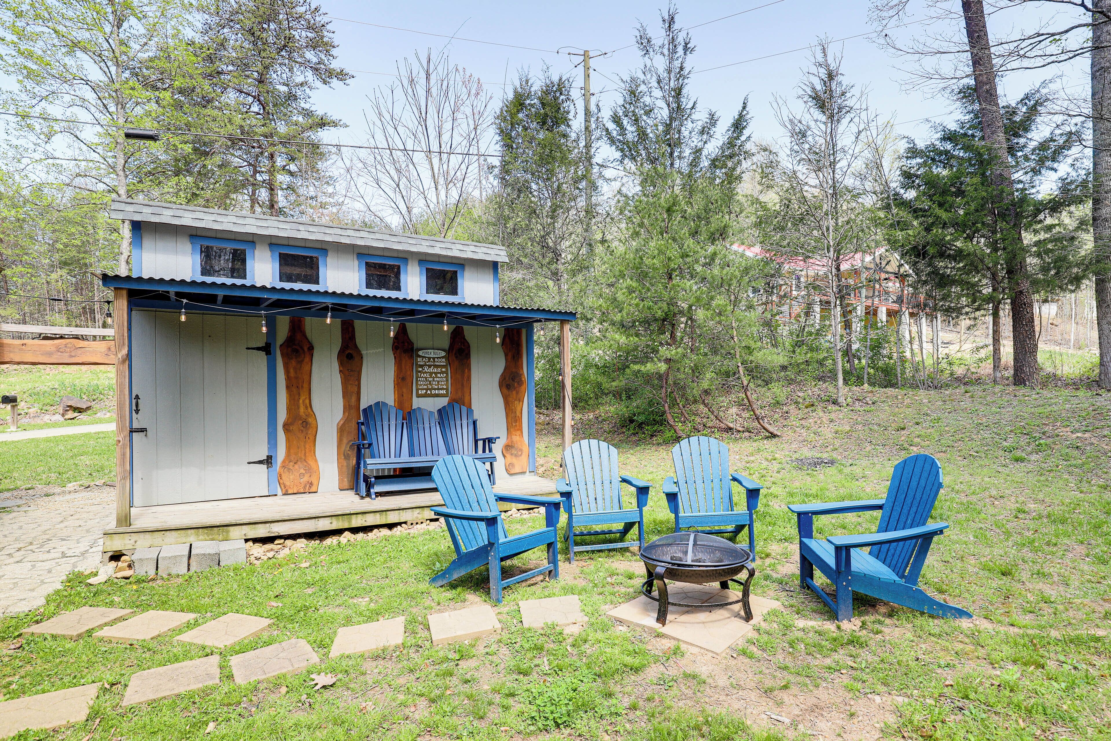 Una pequeña cabaña de madera con un porche, sillas Adirondack azules y un brasero.