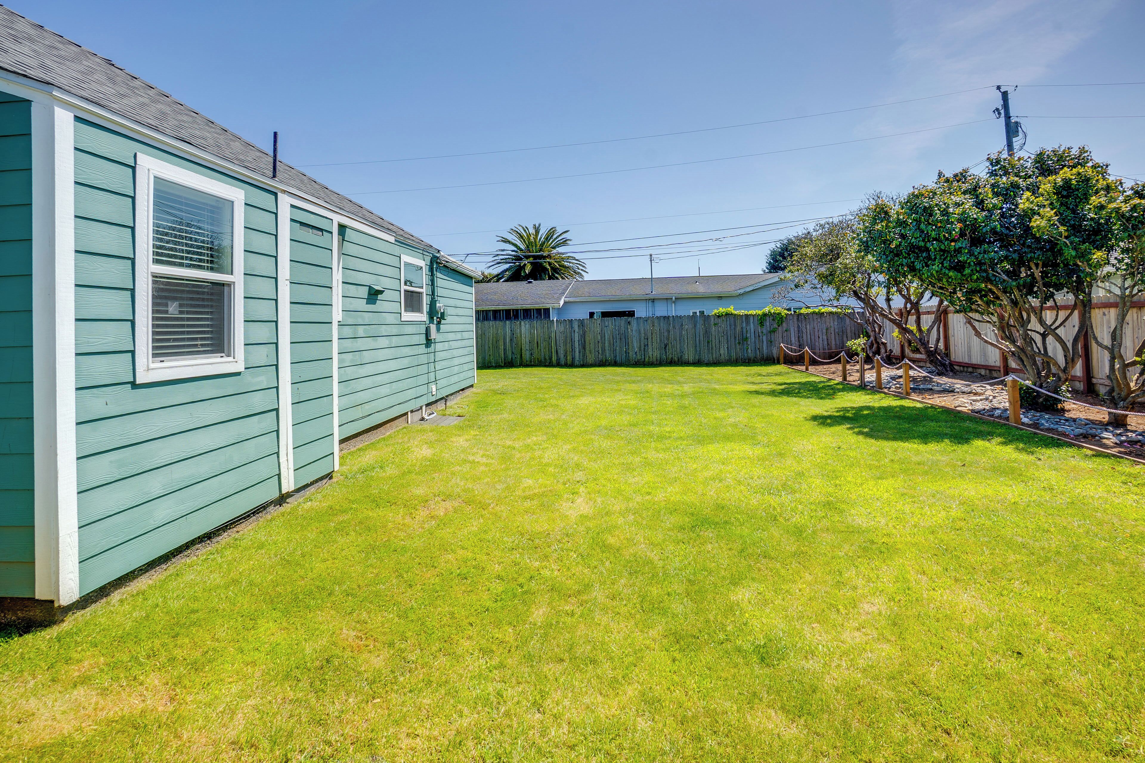 A green house with a fenced yard and a tree.