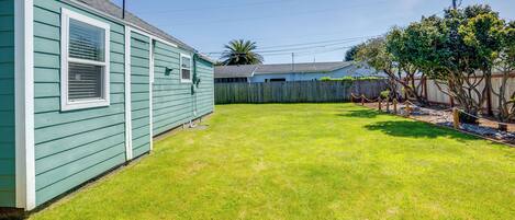 A green house with a fenced yard and a tree.