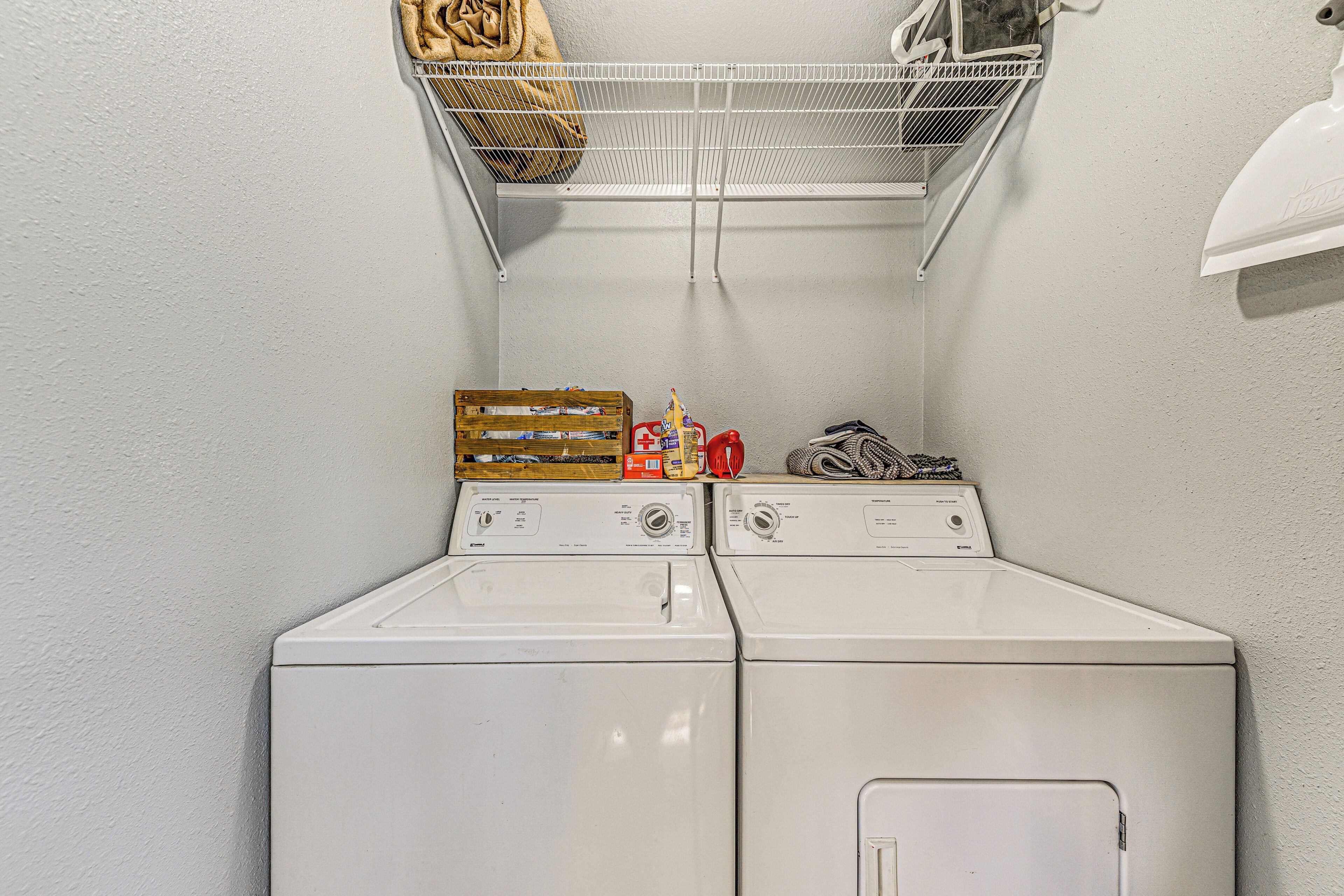 A laundry area with two stacked washers and dryers, a metal shelf above, and a basket hanging on the wall.