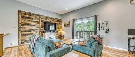 A living room with a sectional sofa, a wooden coffee table, a fireplace, and a large window with a view of greenery.