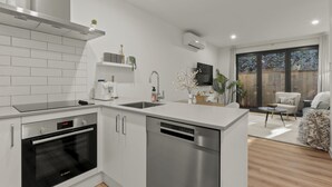 Een moderne keuken met witte kastjes, een Bosch oven en een vaatwasser. Er is een eethoek met een ronde tafel en stoelen, en uitzicht op het landschap door een groot raam.