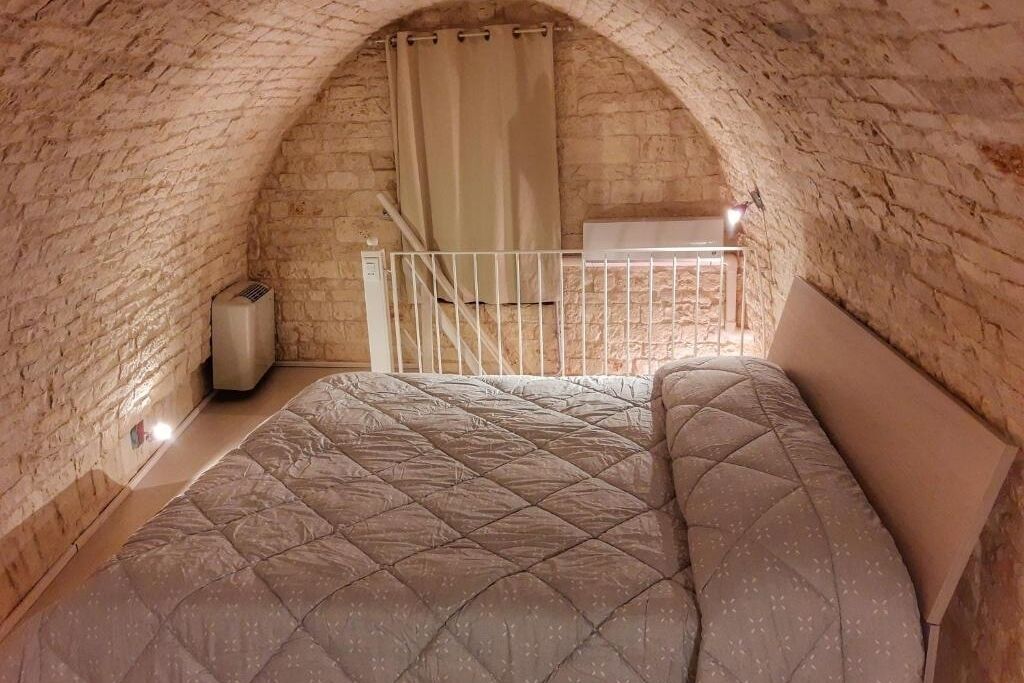 A cozy attic bedroom with a vaulted ceiling, a bed with a quilted mattress, a white railing, and a small heater.
