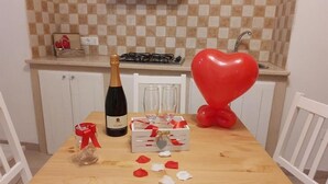 Une cuisine avec un dosseret à carreaux, une bouteille de champagne, des verres, un ballon en forme de cœur et une petite table parsemée de pétales de fleurs rouges et blanches.