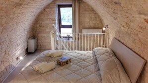 Une chambre à coucher avec un plafond voûté, un lit doté d’un matelas matelassé, une petite table de chevet et une fenêtre donnant sur l’extérieur.
