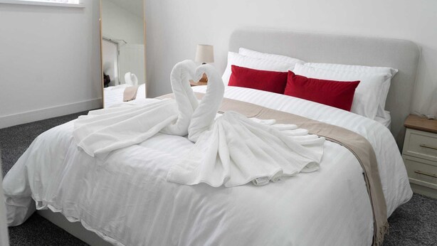 A hotel room with a neatly made bed, a large mirror, and a nightstand with a lamp.