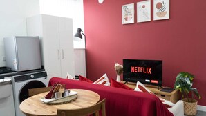 A compact living space with a kitchenette, a dining area, and a seating area with a red sofa and a TV displaying 'NETFLIX'.