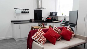 A compact living space with a kitchenette, a sofa with red and white cushions, and a dining area with a small table and chairs.