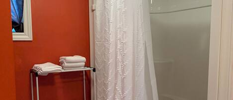A bathroom with a shower, a towel rack with towels, and toilet paper.