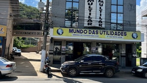 Hotelli nimeltä ”HOTEL MULTILAR”, ja sen vastapäätä on kyltti, jossa lukee ”MUNDO DAS UTILIDADES”.