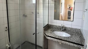 Kylpyhuone, jossa on lasiseinällä varustettu suihku, valkoinen pesuallas ja peili.