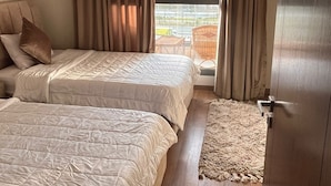 A hotel room with two beds, a view of the city through large windows, and a balcony with wicker furniture. - Luxury Stay (6th of October City)