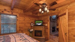 A log cabin interior with a fireplace, a television, and a bed with a patterned bedspread. - Unforgettable Luxury Mountain Getaway (PIGEON FORGE)