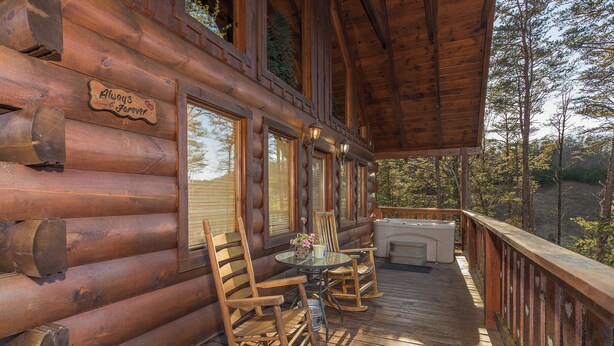 A wooden log cabin with a porch featuring rocking chairs, a table with flowers, and a sign that reads "Always & Forever". - Unforgettable Luxury Mountain Getaway (PIGEON FORGE)