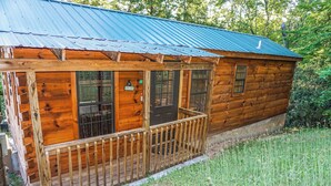 A wooden cabin with a porch, a metal roof, and a 'Welcome' sign.