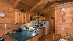 A wooden cabin interior with a kitchen area featuring a stove, microwave, refrigerator, and wooden cabinets.